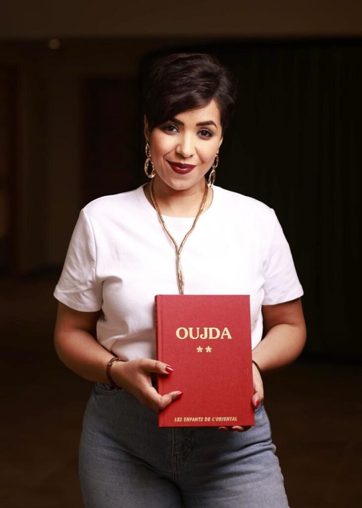 Portrait de Maya Mazroui, CEO d’Evotrust et membre de la diaspora marocaine, tenant un livre rouge intitulé « Oujda »